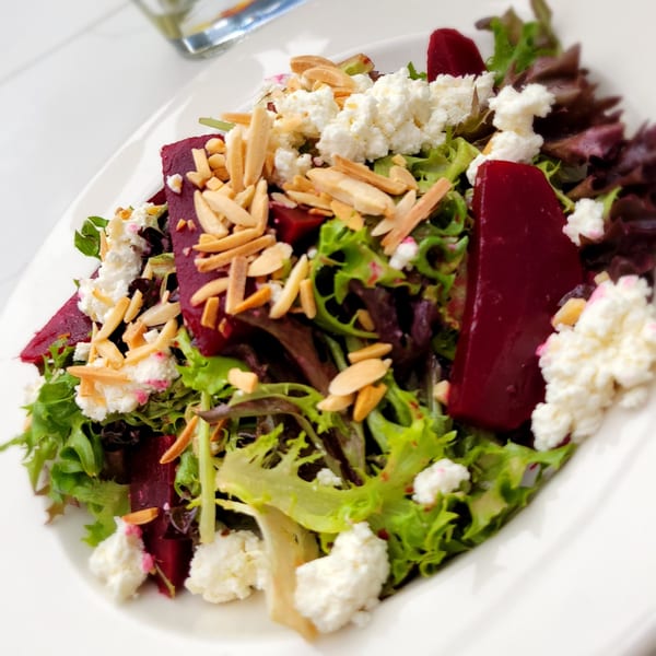 A vibrant beet and goat cheese salad with mixed greens and sliced almonds on a white plate.