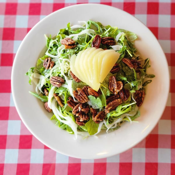 Arugula salad with sliced pears, candied pecans, and shaved fennel on a red and white checkered tablecloth.