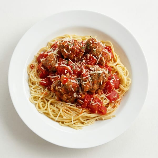Spaghetti with meatballs, tomato sauce, and grated cheese in a white bowl.