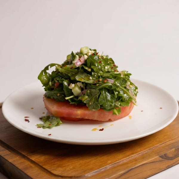 A fresh arugula salad with feta cheese and red onions, served on a thick slice of tomato.