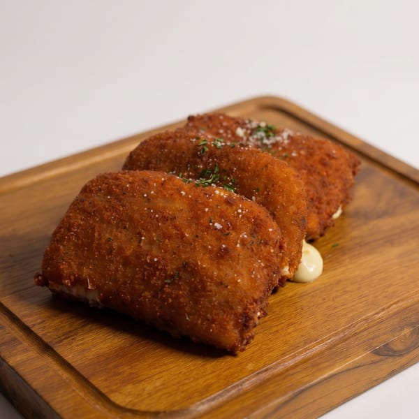 Three golden-brown fried croquettes with herbs and salt, served on a wooden board.