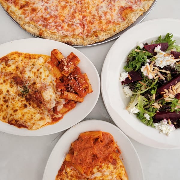 Overhead view of a cheese pizza, baked ziti, rigatoni, and a beet and goat cheese salad.
