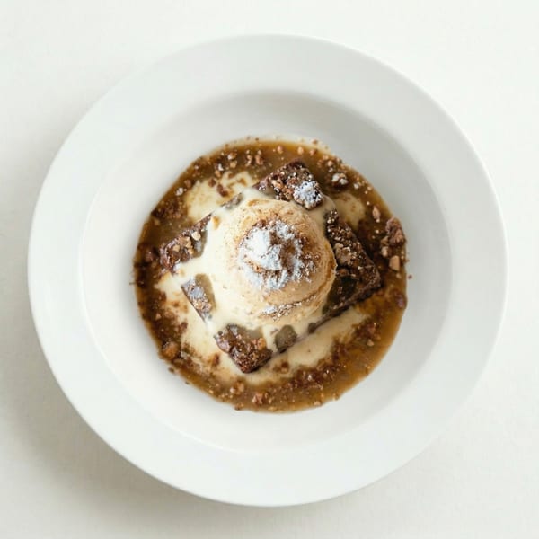 Brownie dessert with a scoop of ice cream, powdered sugar, and caramel sauce in a white bowl.