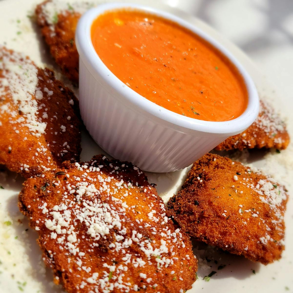 Golden-brown fried ravioli, sprinkled with Parmesan cheese and herbs, served with a side of red marinara sauce.