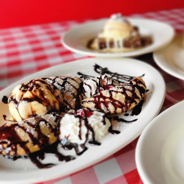 Dessert plate with fried dough, vanilla ice cream, whipped cream, and chocolate syrup on a red checkered tablecloth.