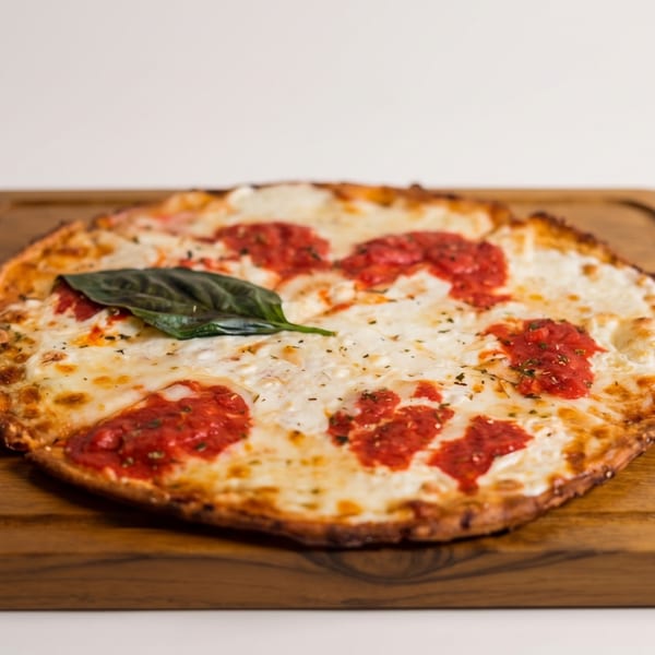 Round Margherita pizza with melted mozzarella, red sauce dollops, and a basil leaf on a wooden board.