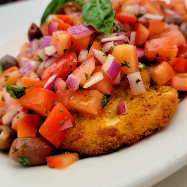 Golden-brown breaded chicken cutlet topped with diced tomatoes, red onions, and olives.
