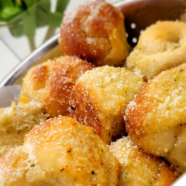 Close-up of golden-brown garlic knots dusted with parmesan cheese and herbs in a metal basket.