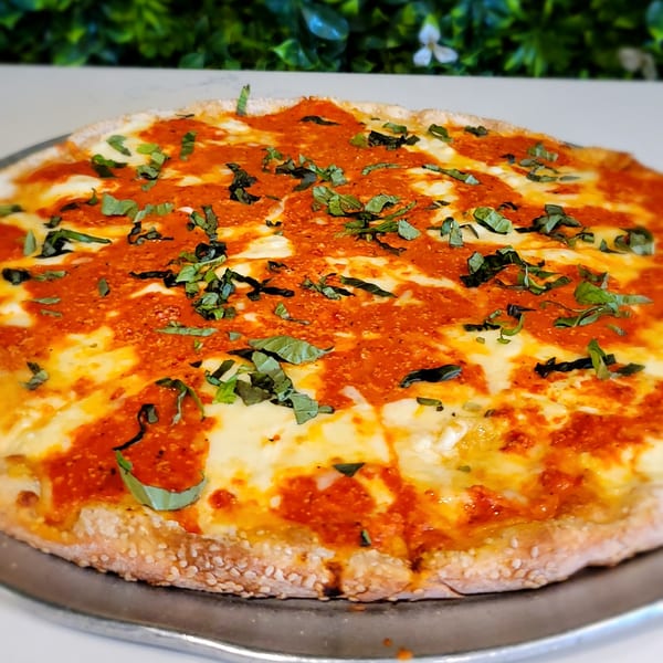A whole round pizza with red sauce, melted white cheese, and fresh green basil on a metal pan.